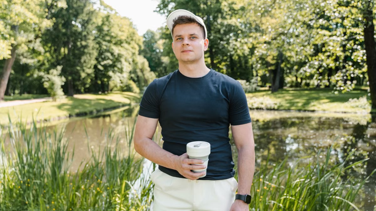 Casual young man in a park, holding a coffee cup. Sunny day in nature.